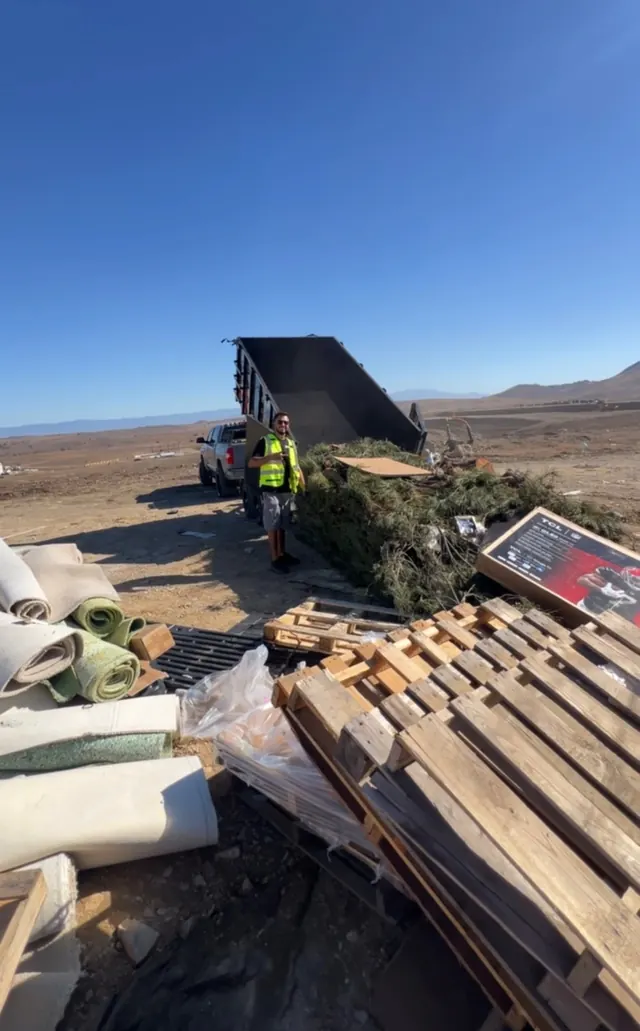 Crew member at a disposal site with pallets, rolled carpet and yard waste
